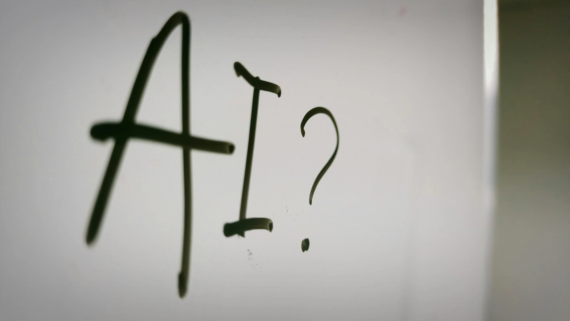 The letters AI and a question mark written in black marker on a whiteboard